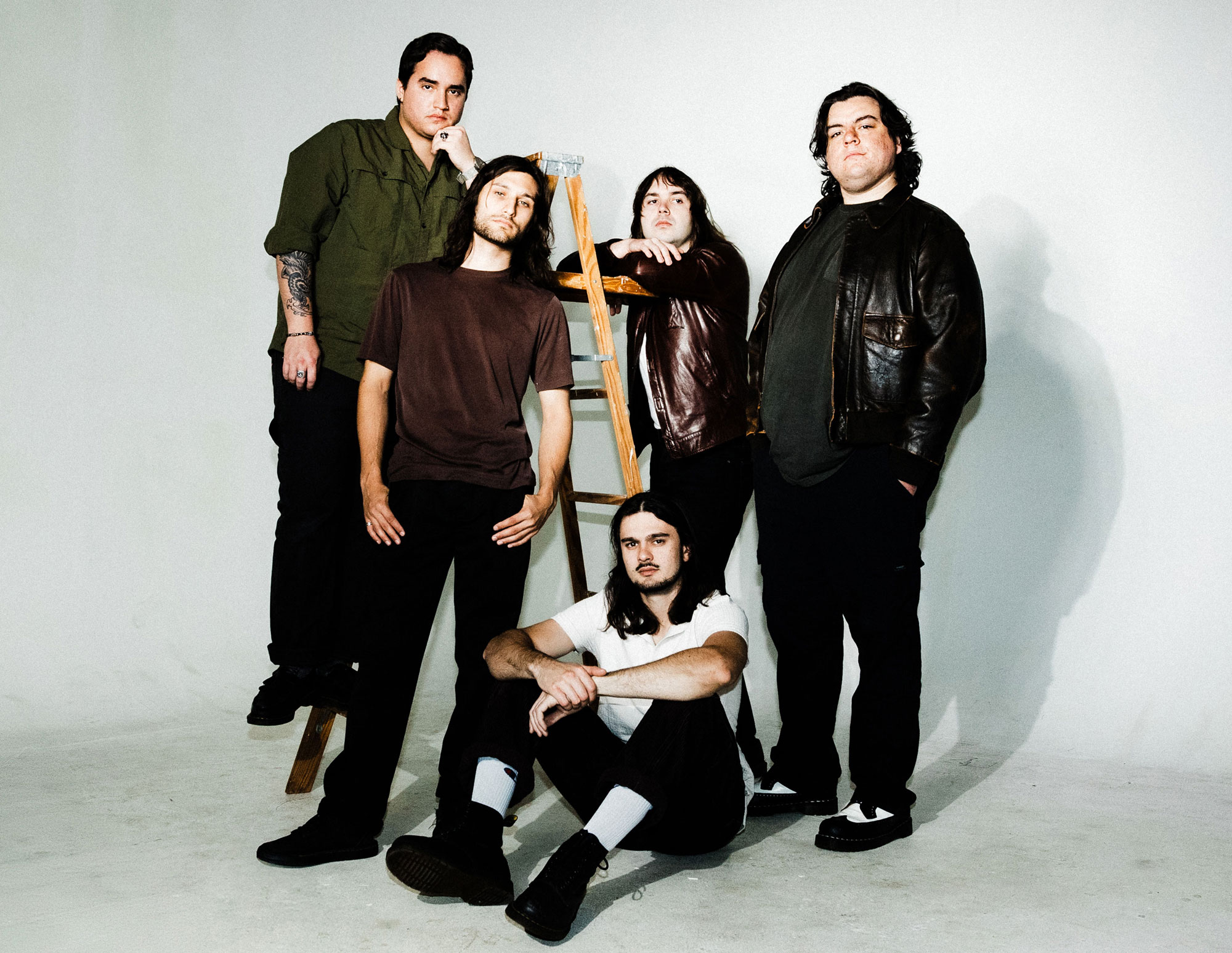 Band grouped together around a wooden ladder, some members on the steps others are leaning against it.